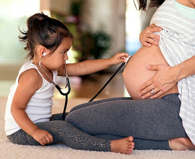 Young girl holding stethescope up to moms pregnant belly